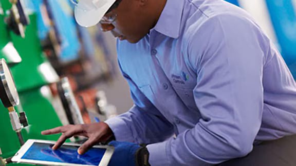 Person in a lab coat using a tablet in an industrial environment.