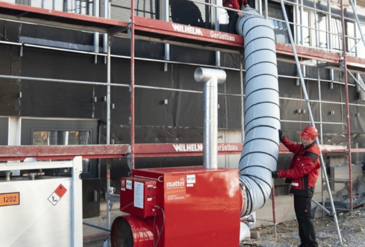 Ein roter Warmlufterzeuger der Marke matter auf einer Baustelle mit einem Bauarbeiter