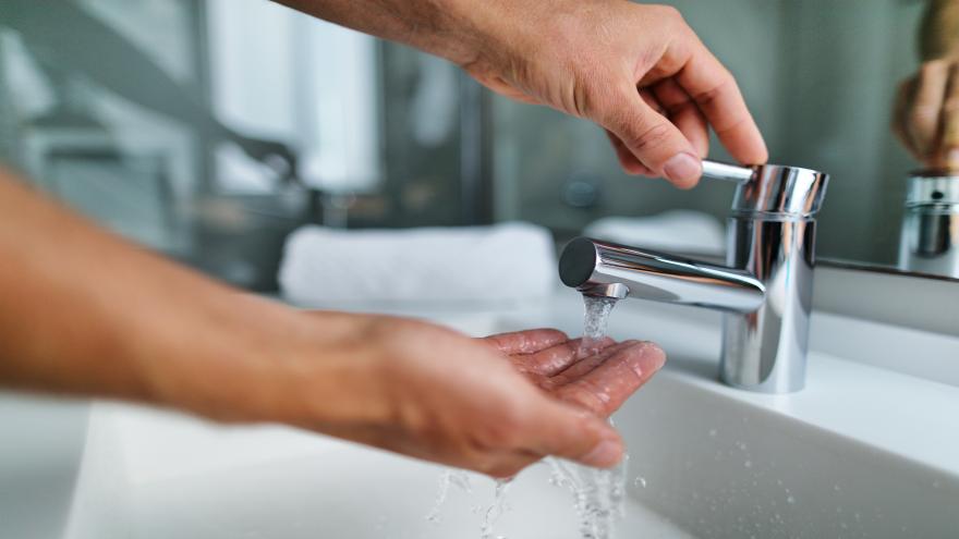 Person, die sich am Waschbecken mit warmen Wasser die Hände wäscht.