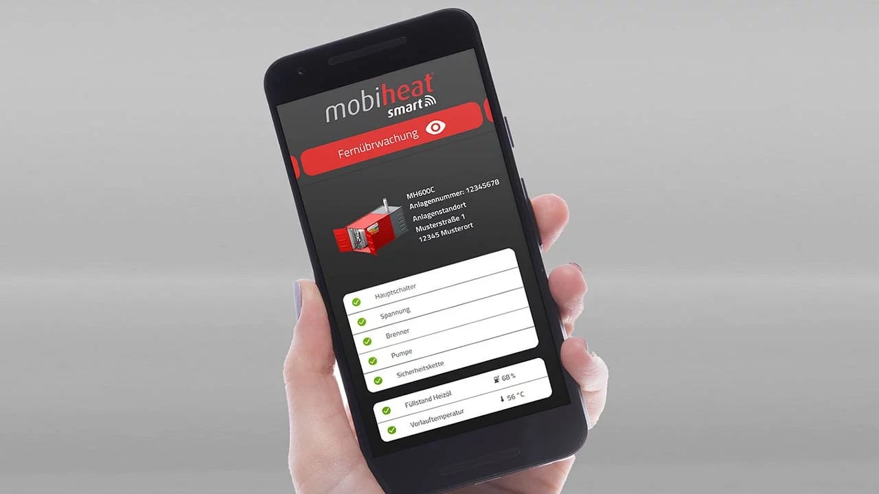 Das Bild zeigt eine Hand, die ein Smartphone hält, auf dessen Bildschirm die "mobiheat smart"-App geöffnet ist. Die App zeigt Informationen zu einem Heizsystem an, darunter die Fernüberwachungsoption, technische Daten (Modell: MH600C, Anlagennummer), Standortinformationen und der Status verschiedener Parameter wie Hauptschalter, Spannung, Brenner und Pumpe, die alle mit grünen Häkchen als aktiv markiert sind. Weiter unten wird der Heizölfüllstand mit 68 % und die Vorlauftemperatur mit 56 °C angezeigt.