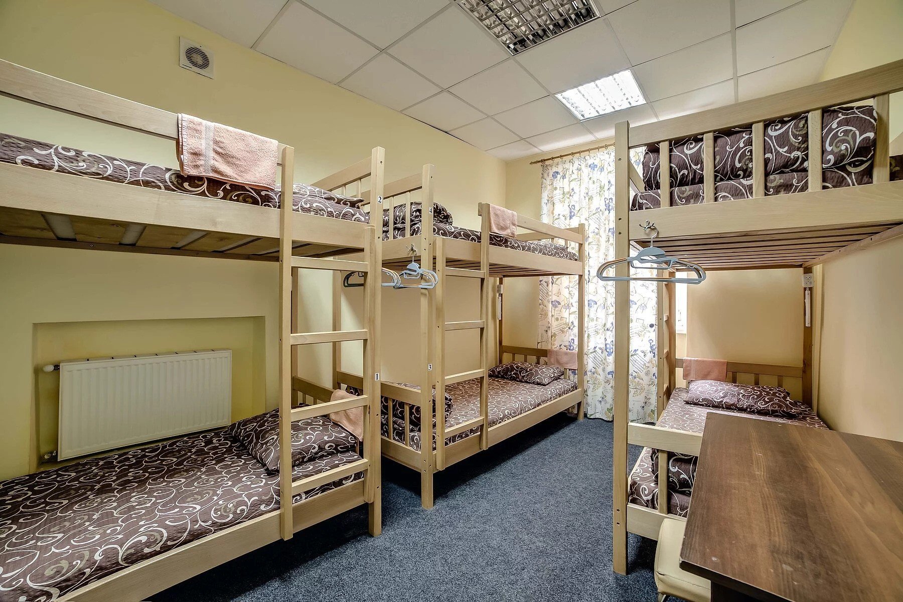 A hostel room with two wooden bunk beds and patterned bedding.