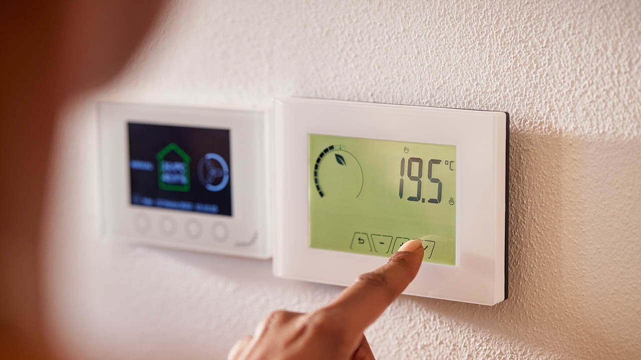 Eine Person berührt ein digitales Thermostat zur Temperaturregelung in einem modernen Wohnraum.